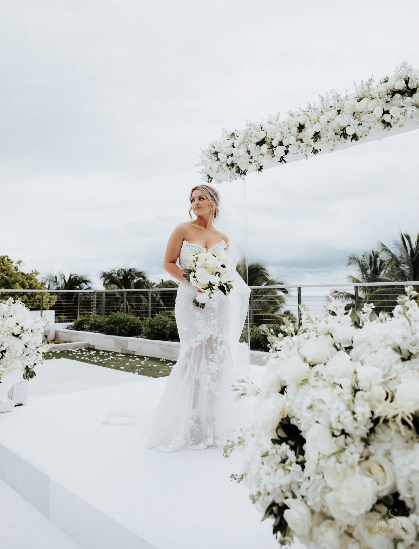 Bride beneath an oceanside white rose ceremony arch