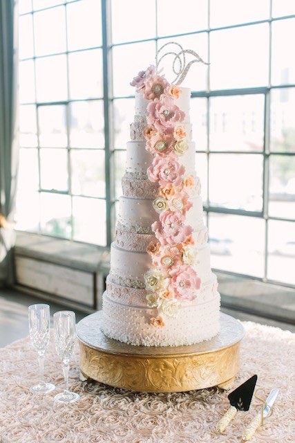 Multi-tier wedding cake with cascading sugar flowers on a gold pedestal