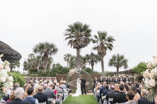 Outdoor ceremony with palm trees and a floral arch by the water