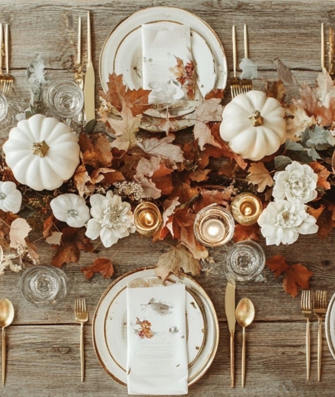 Thanksgiving place settings with white pumpkins, autumn leaves, cream flowers, and gold flatware
