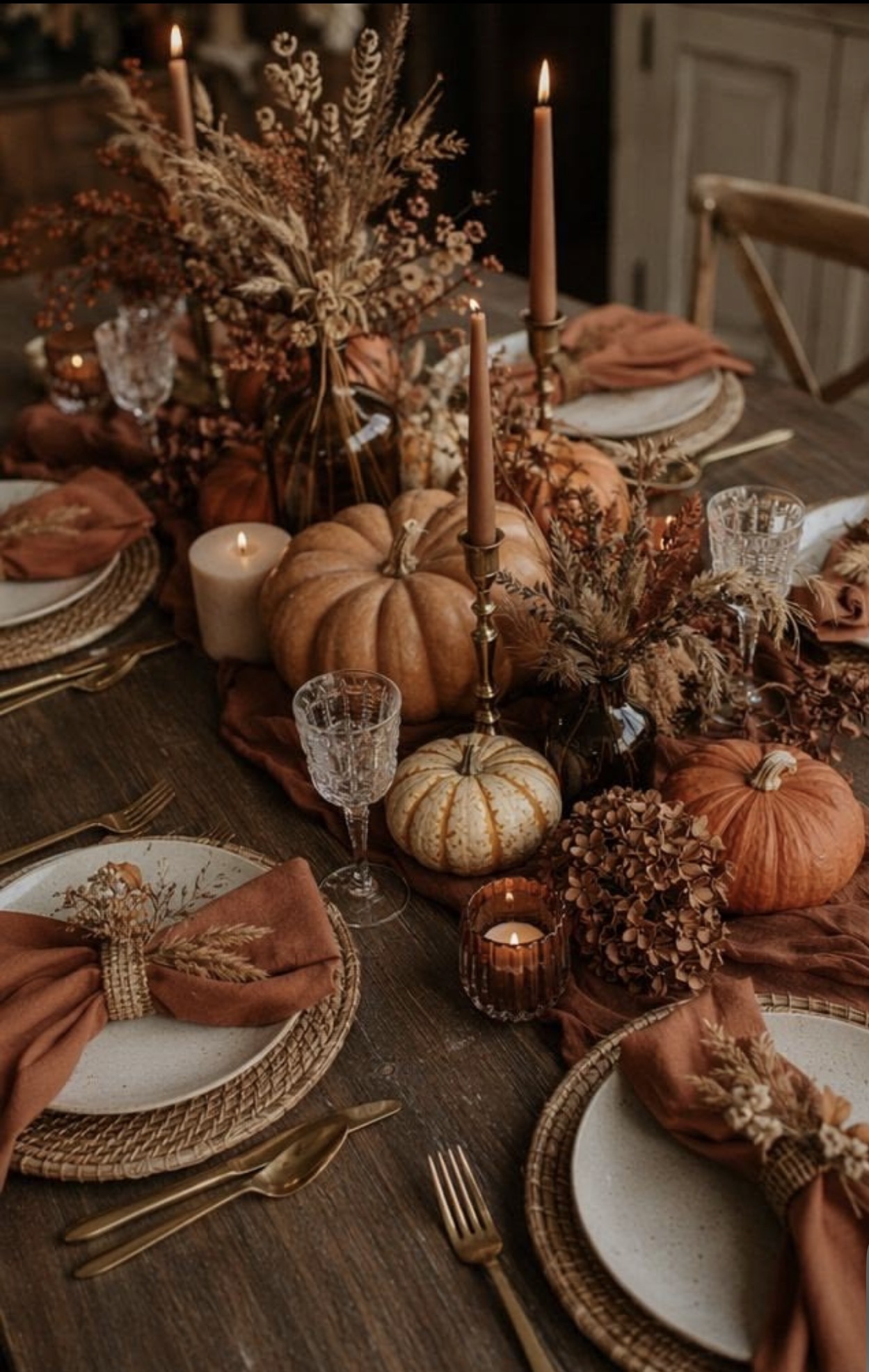 Candlelit Thanksgiving tablescape with heirloom pumpkins, dried botanicals, rust linen napkins, and brass candlesticks