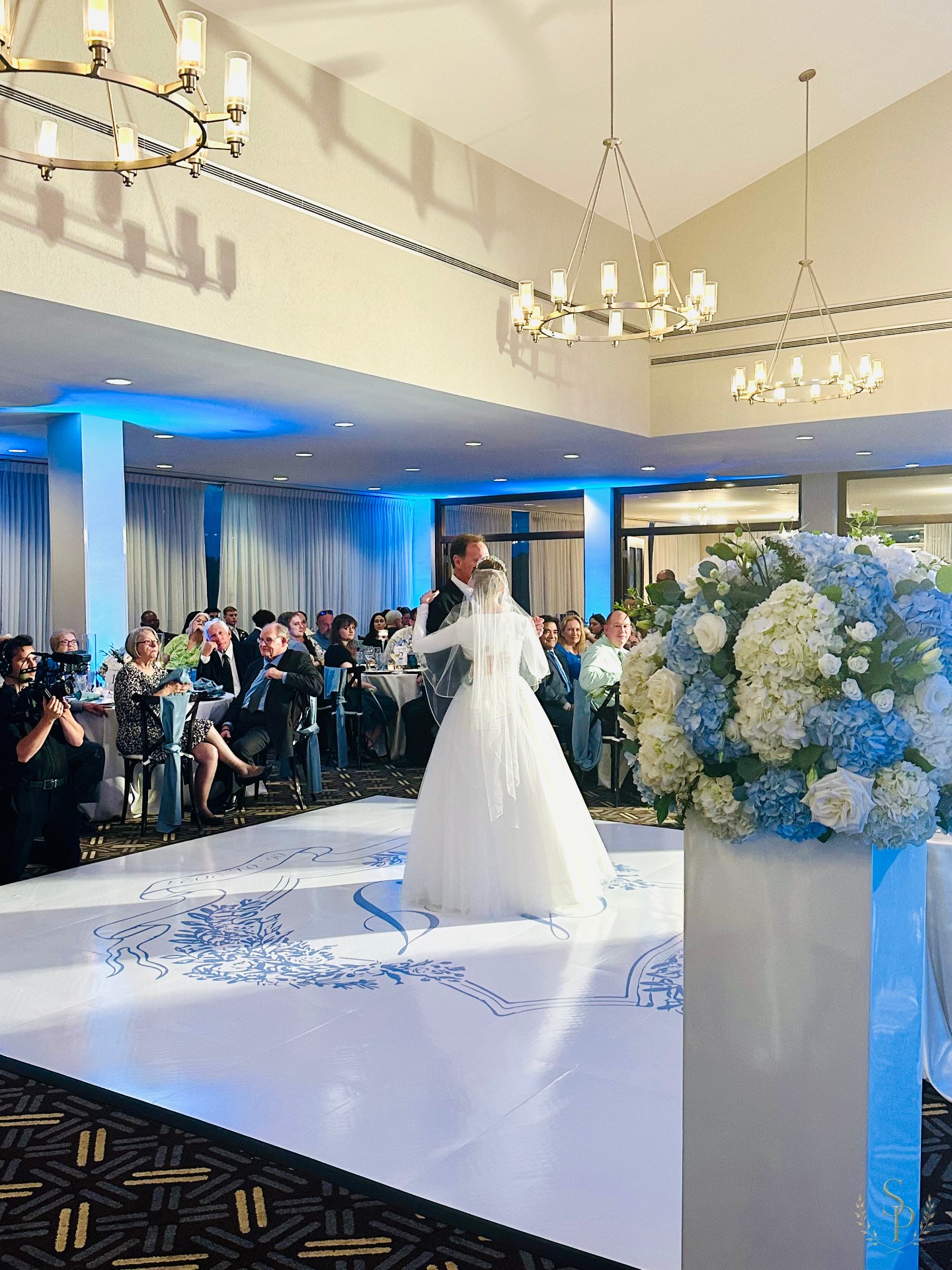 Pedestal arrangement of blue hydrangea and white roses framing the dance floor