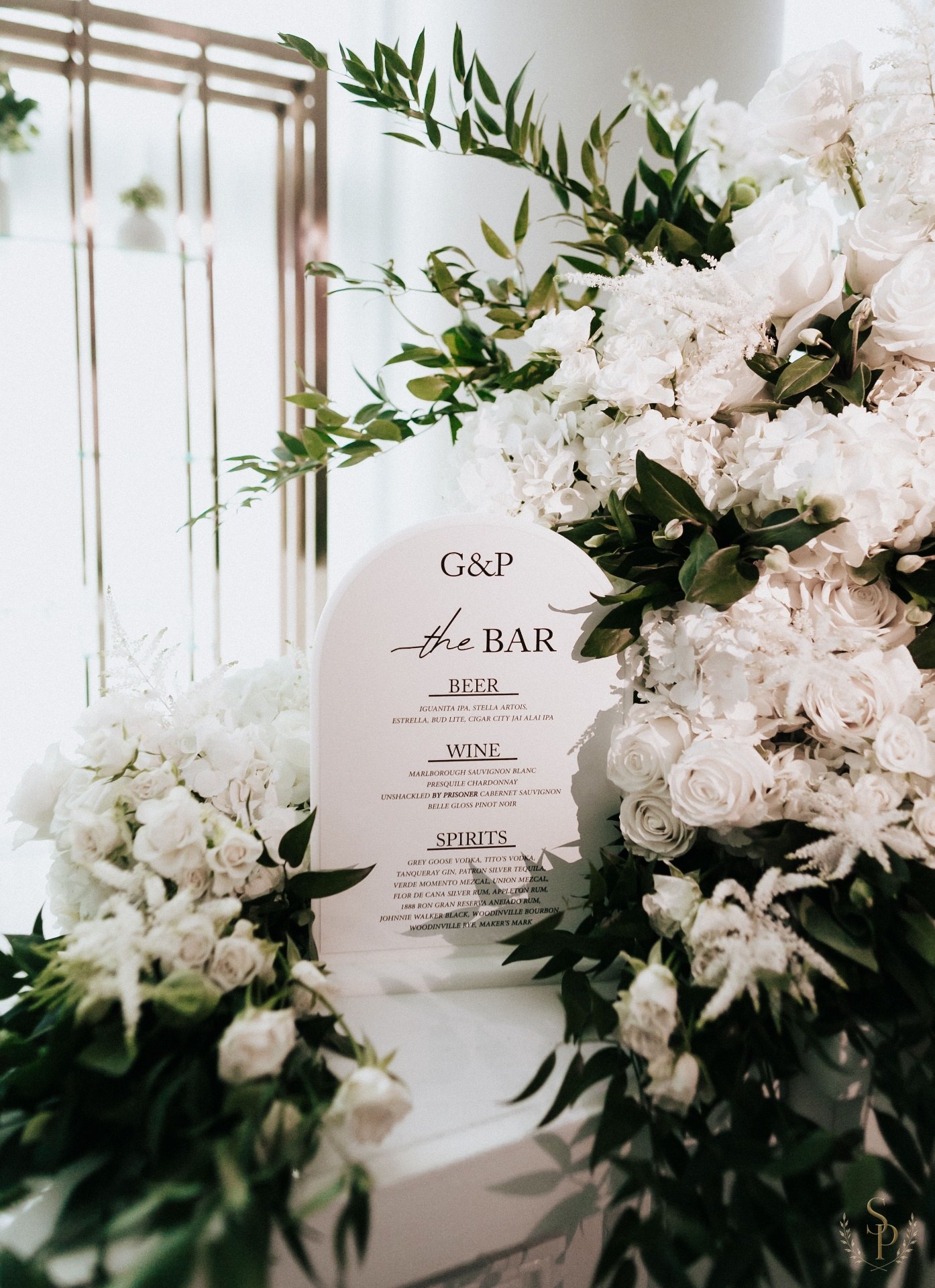 Arched bar menu sign nestled in lush white florals and greenery