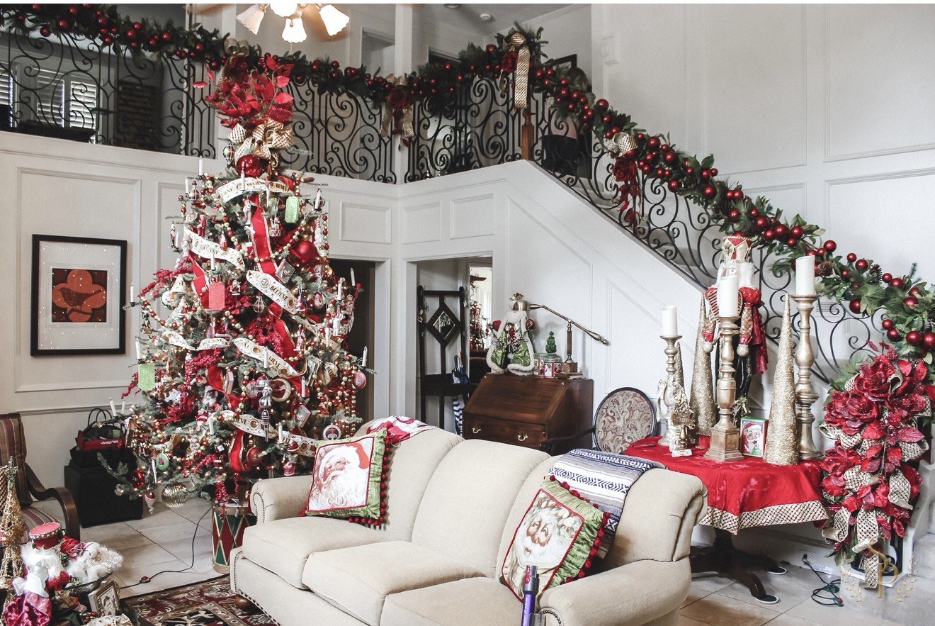 Stair hall filled with red holiday décor, garland, and a richly layered Christmas tree