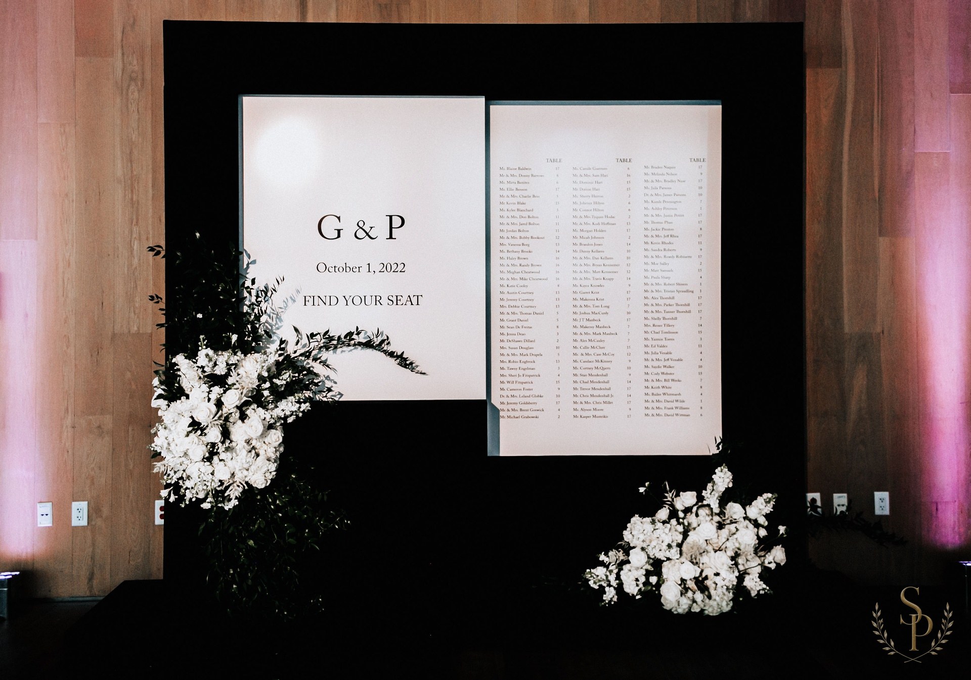 Black-and-white seating chart display flanked by white floral installations
