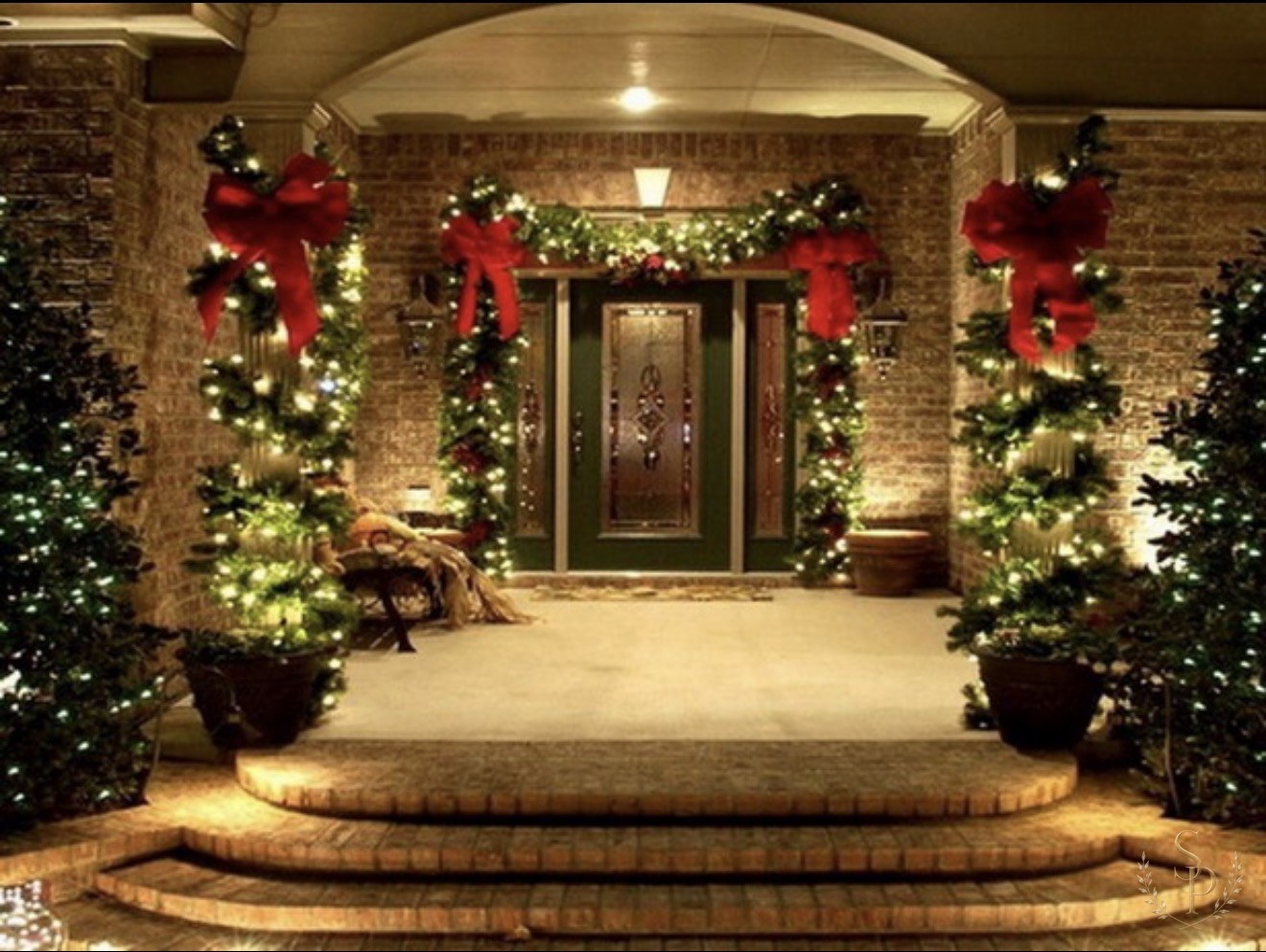 Front porch columns wrapped in lit evergreen garlands and oversized red bows