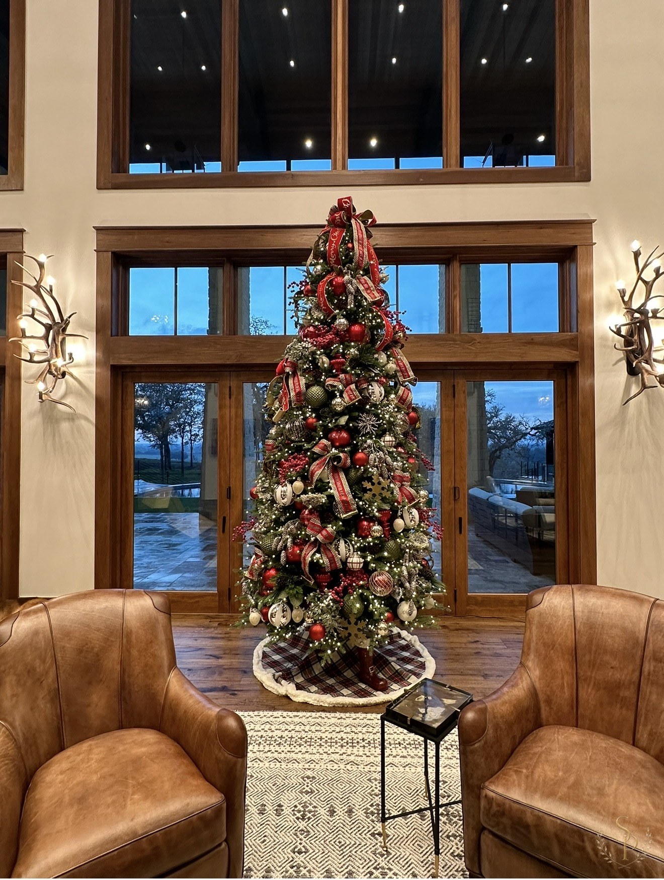 Tall entry Christmas tree framed by wood doors and leather chairs