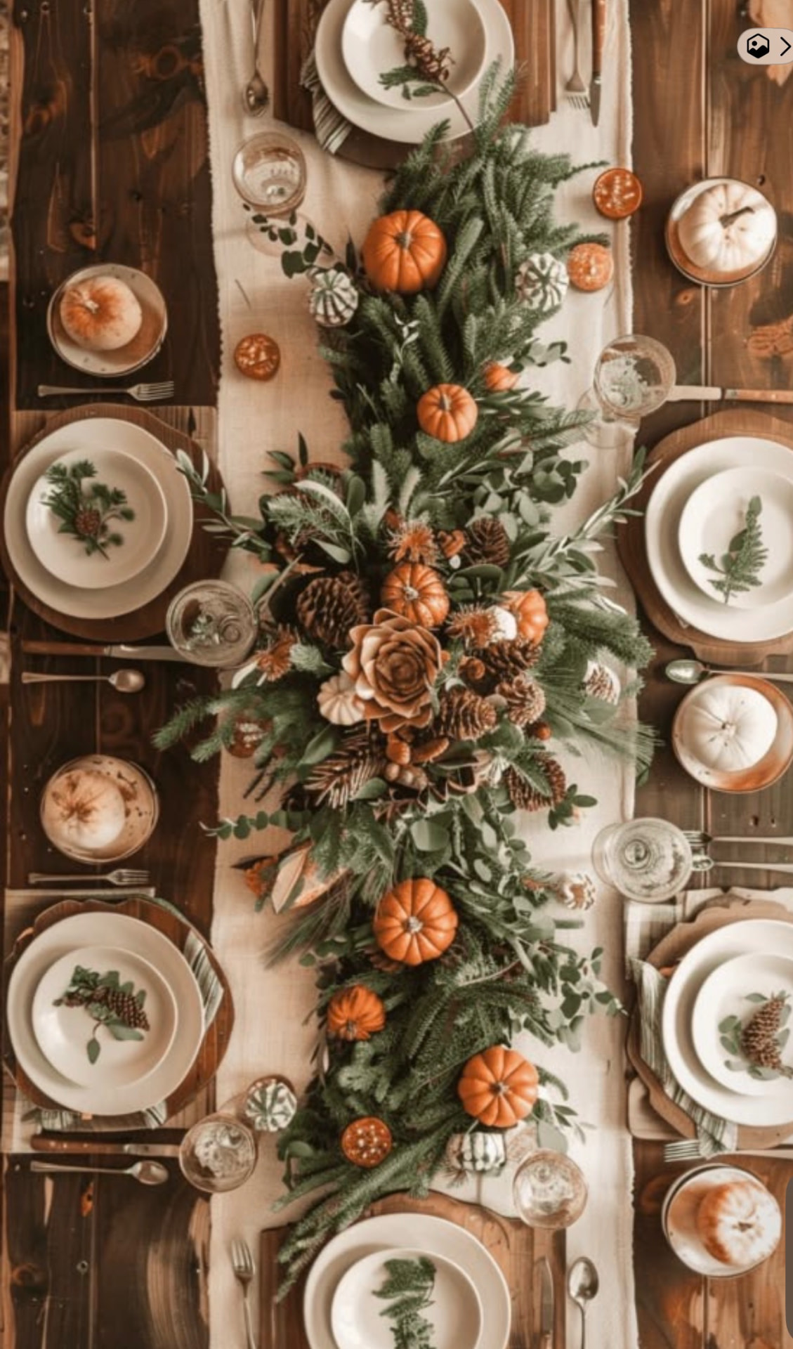 Thanksgiving table with a greenery and mini pumpkin runner, pinecones, and dried oranges