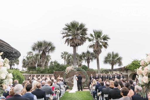 Outdoor ceremony with palm trees and a floral arch by the water