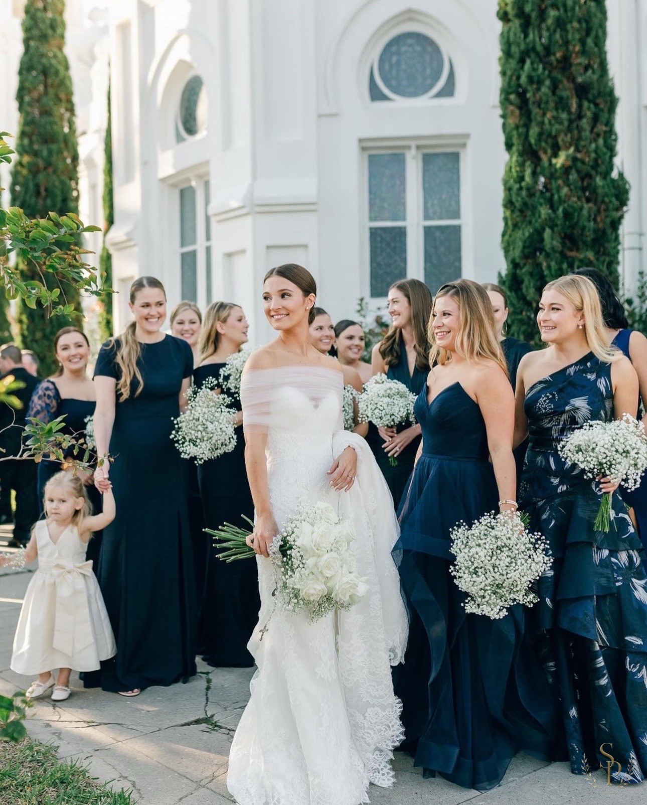 Bride and bridesmaids in navy with white bouquets outside a chapel