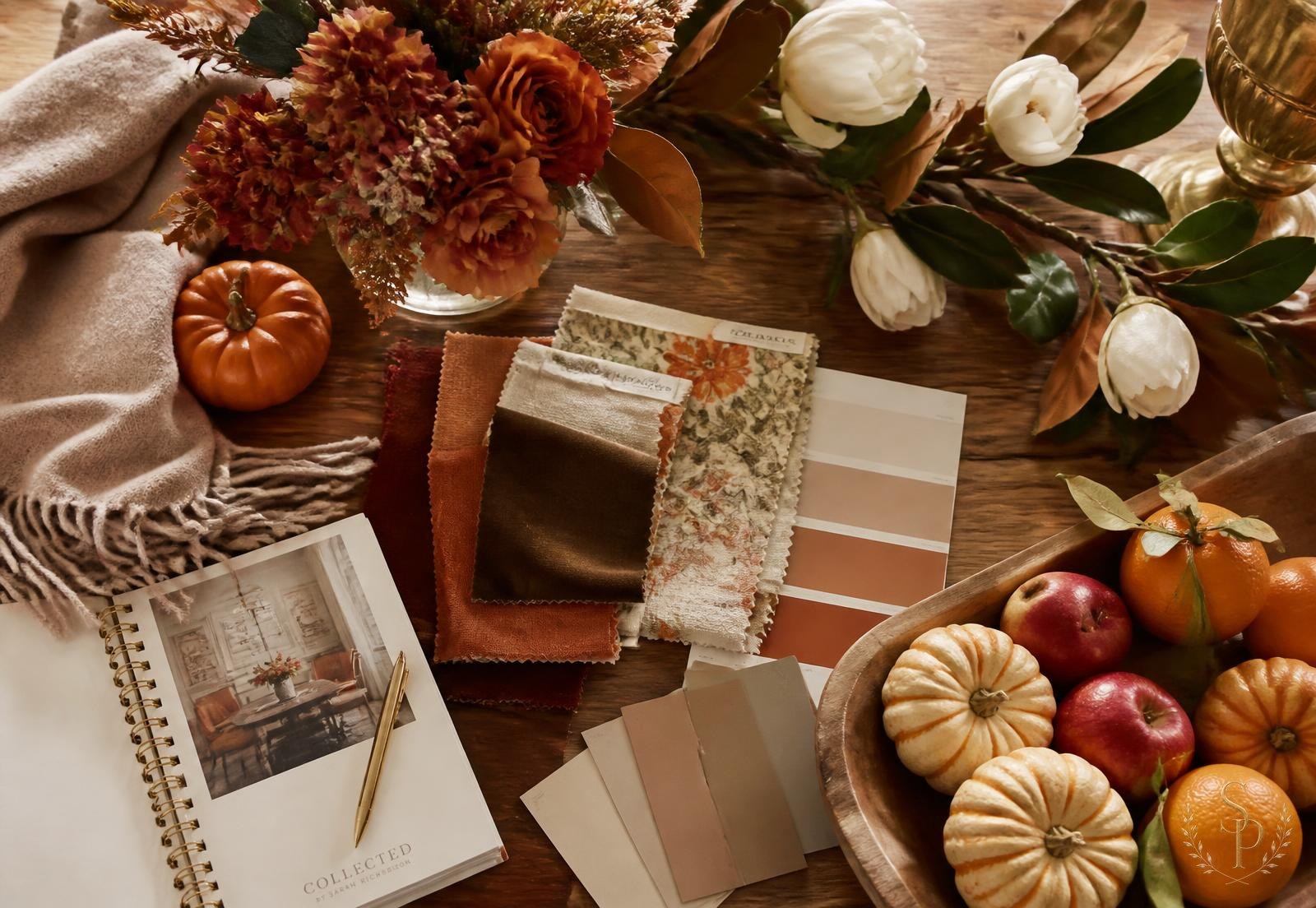 Fall design planning flat lay with rust and brown fabric swatches, silk florals, small pumpkins, apples, oranges, and a soft throw